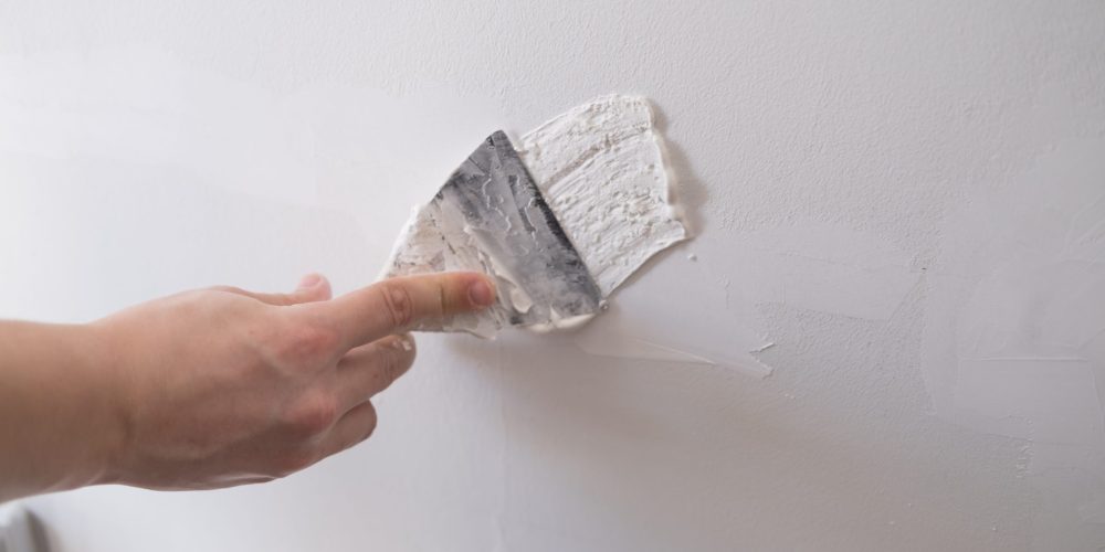 male hand holding a spatula and leveling the walls of the house